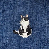 Embroidered patch of a black and white cat on blue denim fabric