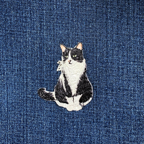 Embroidered patch of a black and white cat on blue denim fabric