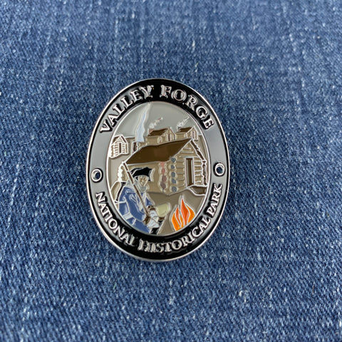 A round enamel Walking Stick Medallion for Valley Forge National Historical Park, featuring a detailed illustration of a soldier and tents on a blue denim background.