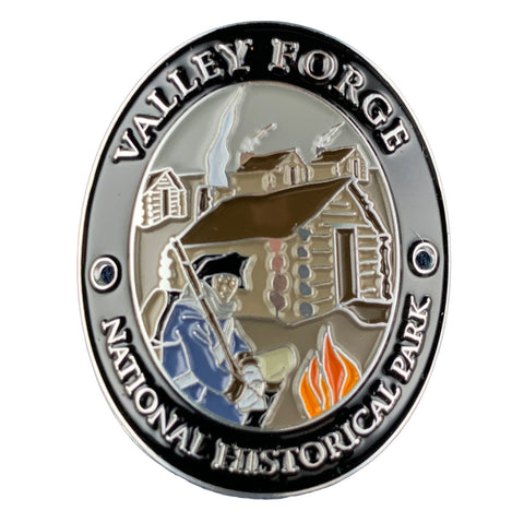 An oval medallion for Valley Forge National Historical Park, featuring a detailed historical illustration of a soldier with a rifle in front of a log cabin and campfire, with the park name engraved around the border.