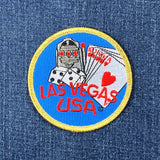 Embroidered circular blue patch with a golden border. Features a slot machine, dice, and a royal flush poker hand over the red text "LAS VEGAS USA" on a denim background