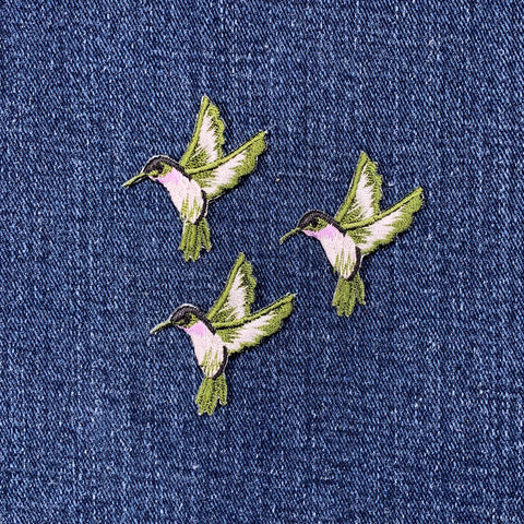 Three embroidered patches depicting violet/green hummingbirds facing left on a denim background