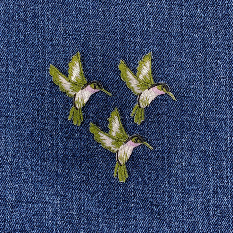 Three embroidered hummingbirds on a denim fabric background