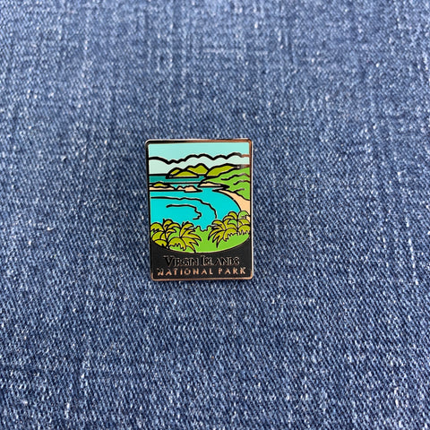 A collectible pin featuring the Virgin Islands National Park with blue waters and green landscapes on a denim background