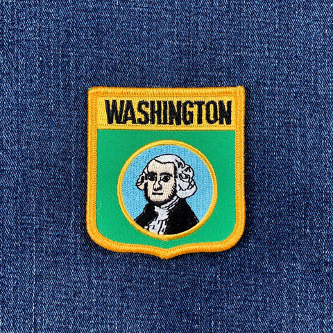A shield-shaped embroidered patch with the text 'WASHINGTON' at the top, a portrait of George Washington in the center, displayed on a denim background.