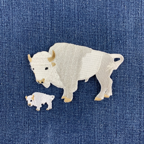 two embroidered patches of white buffalos, one large and one mini, displayed on a blue denim background