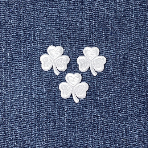 Three white shamrock-shaped patches on a blue denim background