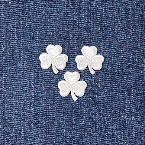 Three small white embroidered shamrock patches on a denim background