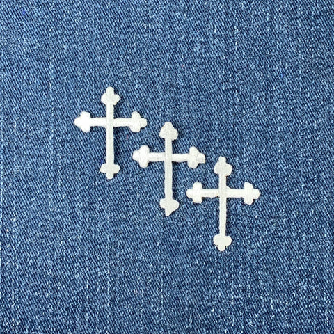 Three white embroidered cross applique patches on a denim background