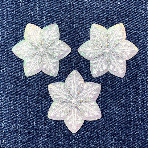 Three star-shaped iridescent snowflake patches on a denim background