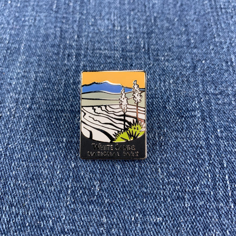 A pin with an illustration of white sand dunes and blue sky, with the text 'White Sands National Park' at the bottom on a denim background.