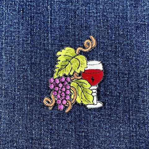 Embroidered patch of a glass of red wine with grapes on denim fabric