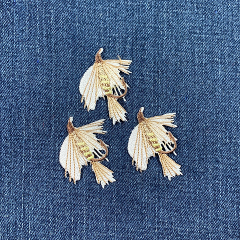 Three embroidered fly fishing lure patches on a denim fabric background