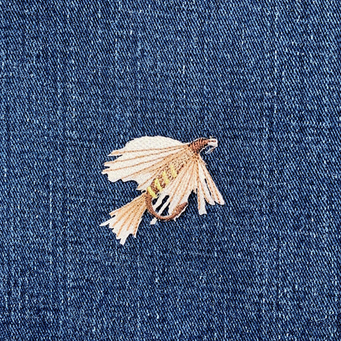 Small fly fishing lure patch on a blue denim fabric background