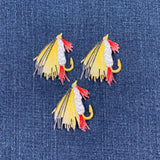 Three embroidered fly fishing lure patches on denim fabric