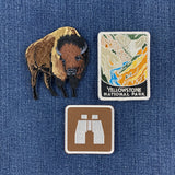three patches: a brown buffalo patch, a Yellowstone national park patch, and a brown binoculars patch displayed on a denim background