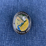 An oval enamel Walking Stick Medallion featuring Yellowstone National Park, displayed on a blue denim fabric background.