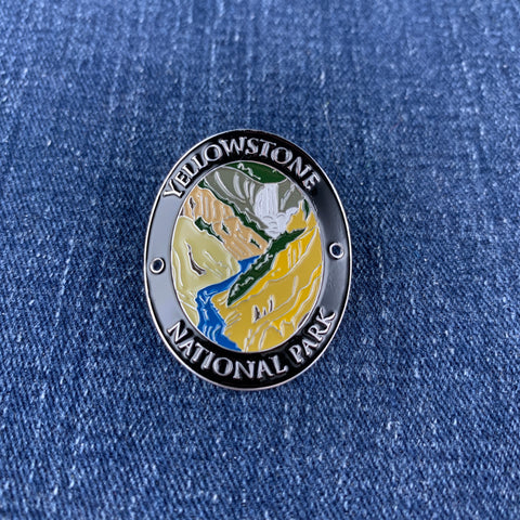 An oval enamel Walking Stick Medallion featuring Yellowstone National Park, displayed on a blue denim fabric background.