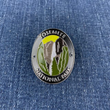 An oval enamel Walking Stick Medallion featuring Yosemite National Park scenery, including the El Capitan and waterfall, with 'YOSEMITE NATIONAL PARK' text, shown on a blue denim background.