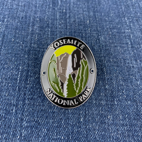 An oval enamel Walking Stick Medallion featuring Yosemite National Park scenery, including the El Capitan and waterfall, with 'YOSEMITE NATIONAL PARK' text, shown on a blue denim background.