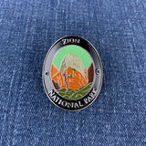 An oval enamel Walking Stick Medallion featuring Zion National Park, displayed on a blue denim fabric background.