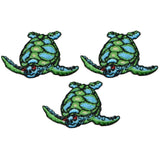 Three embroidered patches depicting mini sea turtles facing left, in shades of green and blue, designed to be ironed onto fabric.