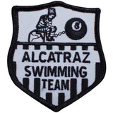 A shield-shaped patch with the text 'Alcatraz Swimming Team' and an illustration of a figure in a straight jacket and an 8-ball.