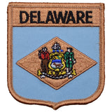 A shield-shaped embroidered patch with the text 'DELAWARE' at the top, featuring an emblem in the center, and a beige and blue color scheme.