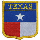 A shield-shaped embroidered patch with the Texas state flag colors and the word 'TEXAS' across the top. The patch has a yellow outer edge, with blue, red, and white fields and a white star.