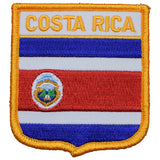 A shield-shaped embroidered patch with the words 'COSTA RICA' across the top. The patch features horizontal stripes of blue, white, and red with a central emblem of Costa Rica.