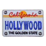 A patch designed to resemble a California license plate with 'Hollywood' written on it, featuring a white background with blue and red text, and decorative elements such as a sun motif.