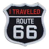 A shield-shaped patch with the text 'I TRAVELED ROUTE 66' on a black background with red and white lettering.