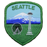 A shield-shaped patch featuring the Seattle skyline with the Space Needle and a representation of Mount Rainier in the background. The patch has a blue sky, green field at the bottom, and includes the text 'SEATTLE'.