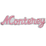 A pink, iron-on embroidered patch that reads 'Monterey' in a cursive font on a white background