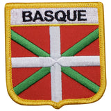 A shield-shaped embroidered patch with the text 'BASQUE' on it, featuring a red and white cross with a green diagonal band, bordered by a yellow edge.