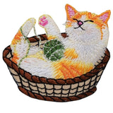 Embroidered patch of a cat inside a basket, with the cat depicted in white, orange, and yellow colors, looking relaxed with a yarn ball beside it.