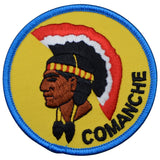 A round patch featuring an illustration of a Native American figure with a headdress, predominantly yellow with red and black accents, and the word 'COMANCHE' below.