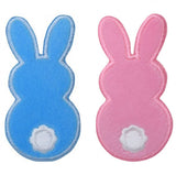 Two embroidered patches in the shape of rabbits, one blue and one pink, with a white belly spot, designed to be ironed onto fabric.