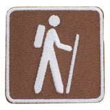 A square-shaped embroidered patch with an illustration of a hiker on a brown background, designed as a badge for hiking activities.