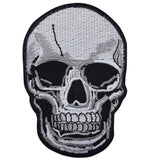 A black gray and white embroidered patch in the shape of a human skull head skeleton.