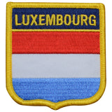 A shield-shaped embroidered patch with the text 'LUXEMBOURG' on it, featuring horizontal stripes of red, white, and blue, bordered with a yellow edge.