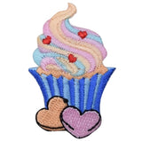 A embroidered patch depicting a cupcake with heart-shaped sprinkles on it, with an 'iron on' backing.