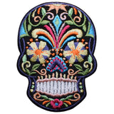A colorful embroidered patch in the shape of a sugar skull, featuring floral patterns and a skeleton design for Dia de los Muertos and Halloween.