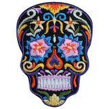 A colorful embroidered patch in the shape of a sugar skull, designed as a Dia de los Muertos or Halloween badge.
